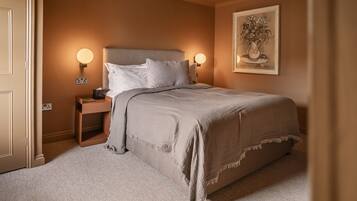A bedroom with a large bed, two bedside tables, a nightstand, a wall-mounted lamp, and a framed artwork.