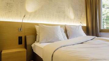 Una cama bien hecha con sábanas y almohadas blancas, un cabecero con textura y una mesita de noche con lámpara.