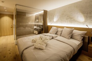 Quarto de hotel moderno com uma cama grande, chuveiro amplo, toucador com espelho e parede com textura.