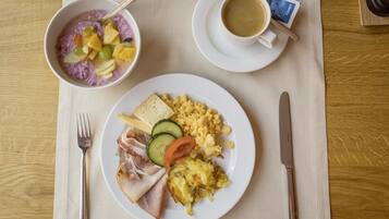 A breakfast setting with a bowl of fruit, scrambled eggs, and a plate of meats and vegetables.