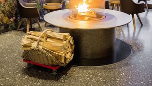 Un interior moderno con una chimenea de piedra central, zona de estar y vistas a montañas nevadas a través de grandes ventanales.