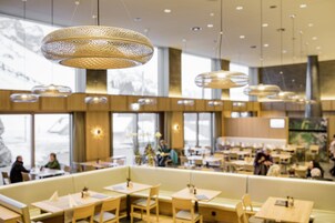 Interior moderno de restaurante con techos altos, lámparas colgantes y una variedad de opciones de asientos, incluyendo cabinas y mesas.
