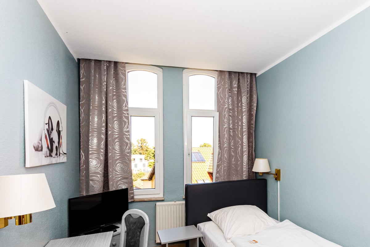 A hotel room with a bed, a desk, a chair, a TV, a lamp, and a window with curtains.