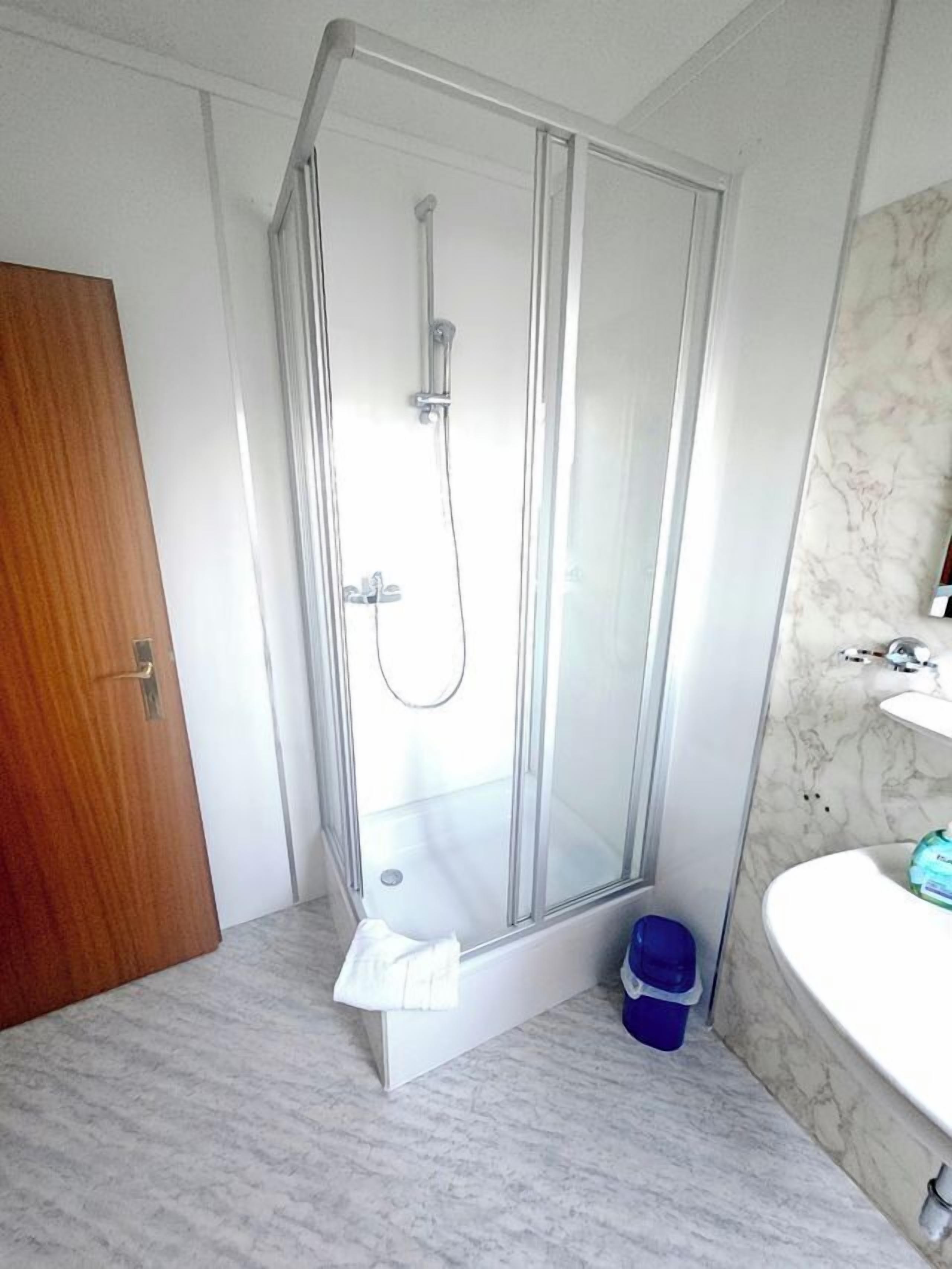 Ein Badezimmer mit Duschkabine, Holztür, Marmorwaschtisch und blauem Mülleimer.