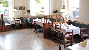 Ein Restaurant mit Boxsitzgelegenheiten, weißen Tischdecken und hängenden Pendelleuchten.