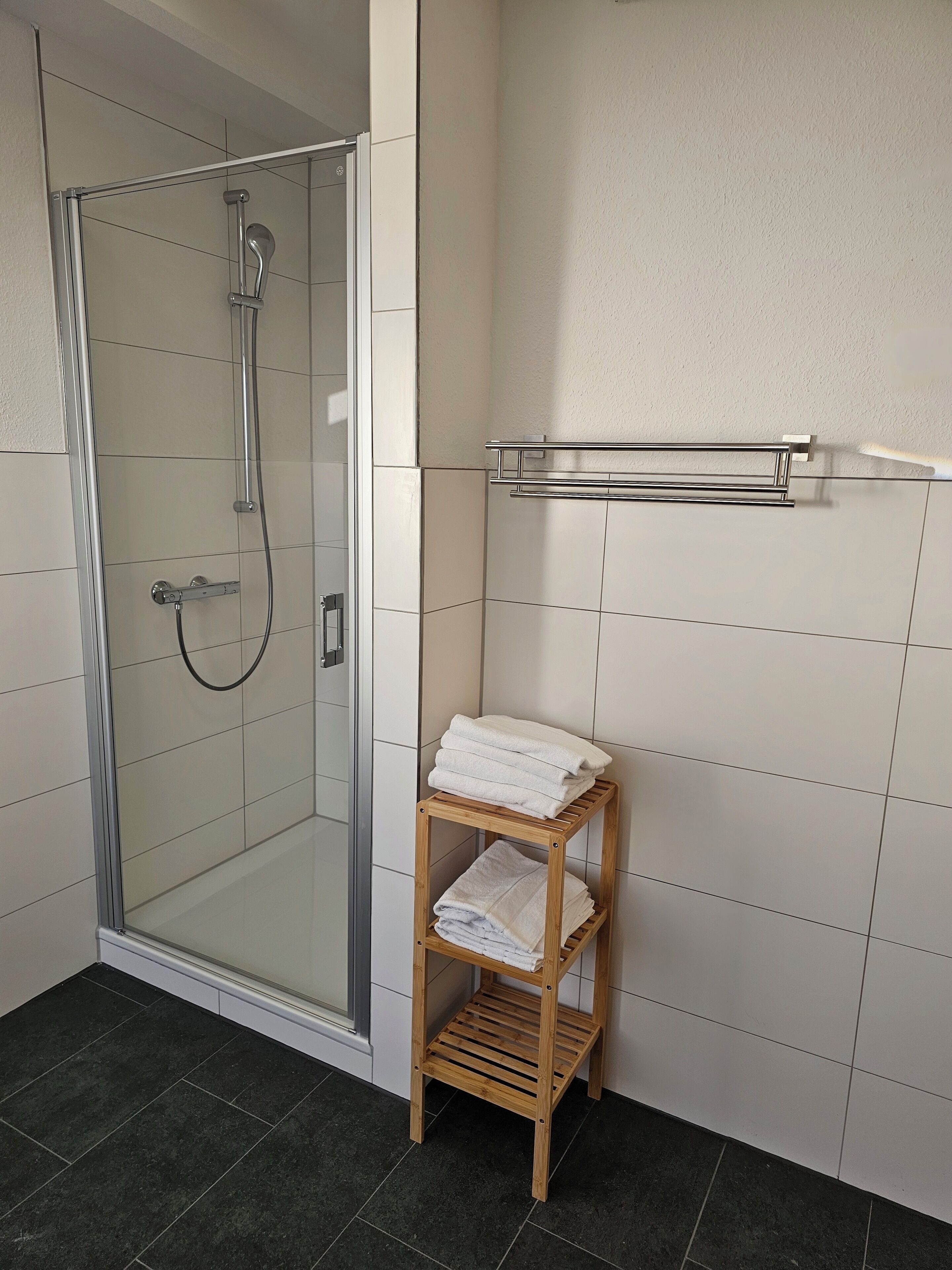 Ein Badezimmer mit einer gläsernen Duschkabine, einer Holzwand mit gefalteten Handtüchern und einem Handtuchhalter an der Wand.