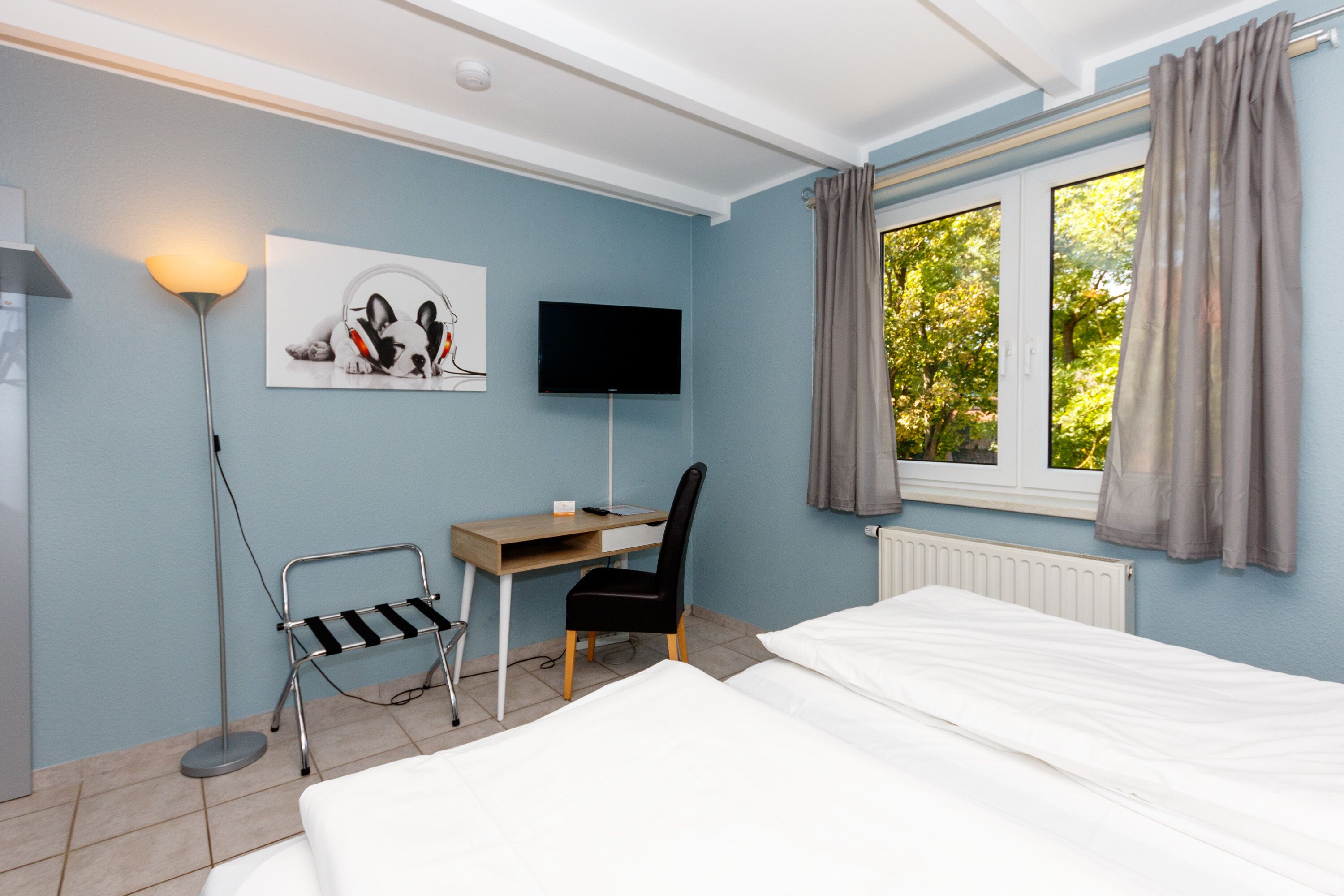 A hotel room with a bed, desk, chair, and a TV on the wall.