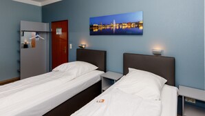 Ein Hotelzimmer mit zwei Einzelbetten, einem Kleiderschrank, einem Spiegel, einem Stadtbild und einem Nachttisch mit einer Lampe.