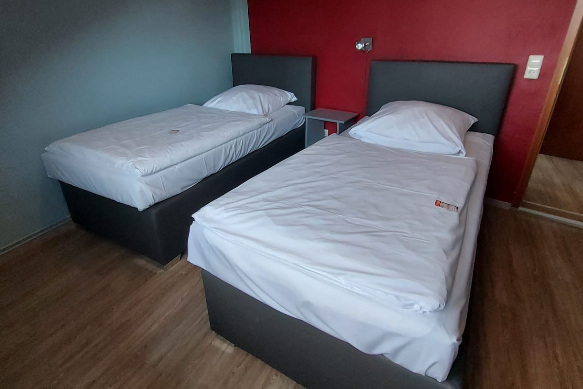 A room with two single beds and a double bed, wooden flooring, and red walls.