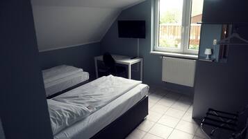 A dormitory room with two beds, a desk, a chair, a TV, and a window with a view of the outside.