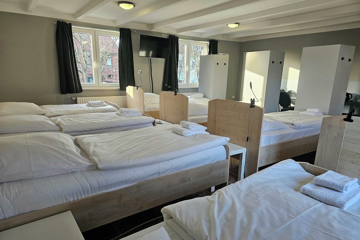 A hotel room with multiple beds, a flat-screen TV, and a window with curtains.