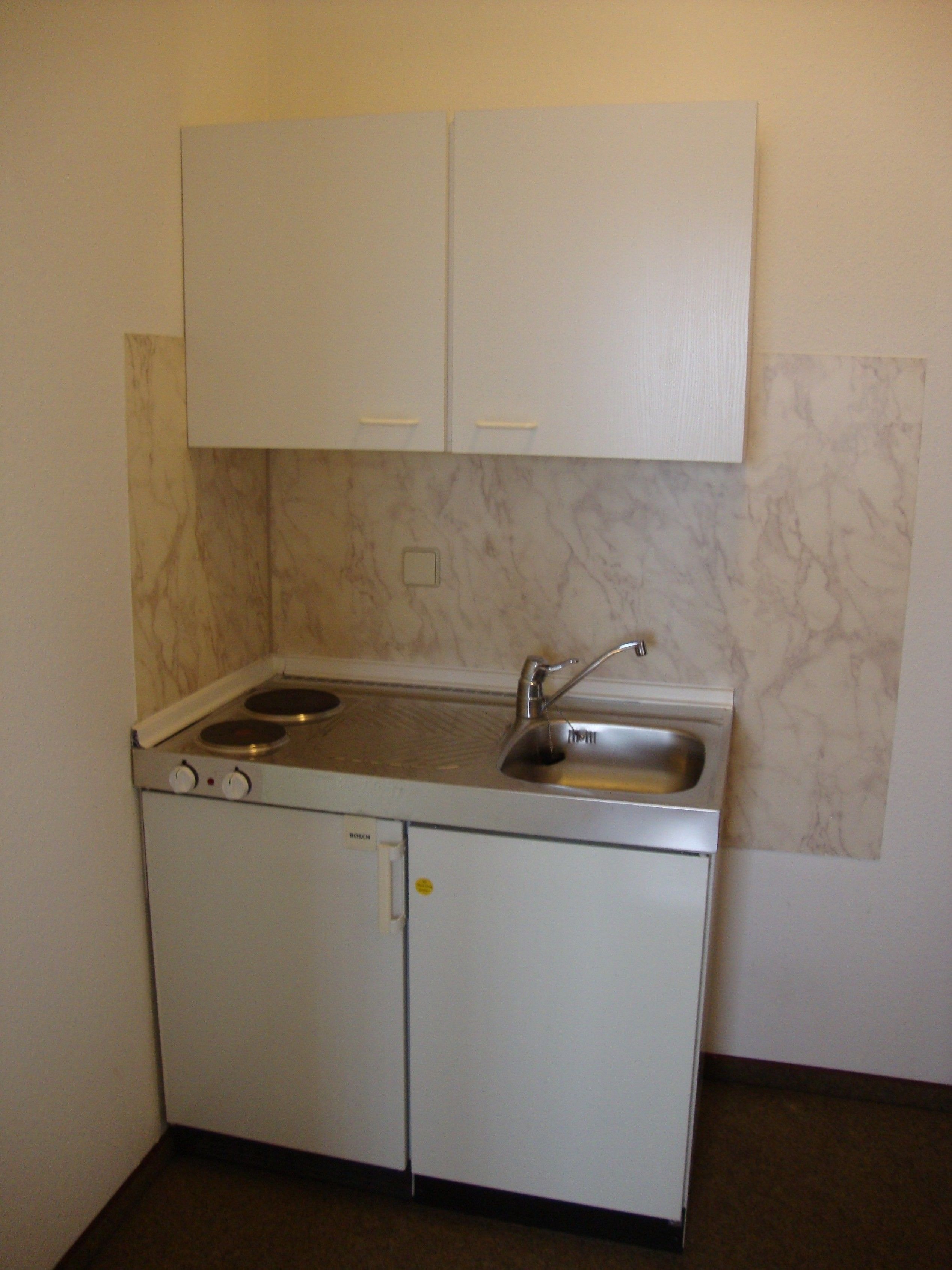 Een kleine keuken met witte kastjes, een inbouwfornuis en een spoelbak.