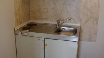 Een kleine keuken met witte kastjes, een inbouwfornuis en een spoelbak.