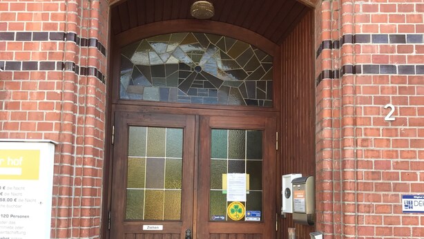 Ein Backsteinhaus mit einer hölzernen Doppeltür, einem kleinen Eingang mit Stufen und einem Schild mit der Nummer 2 an der Wand.