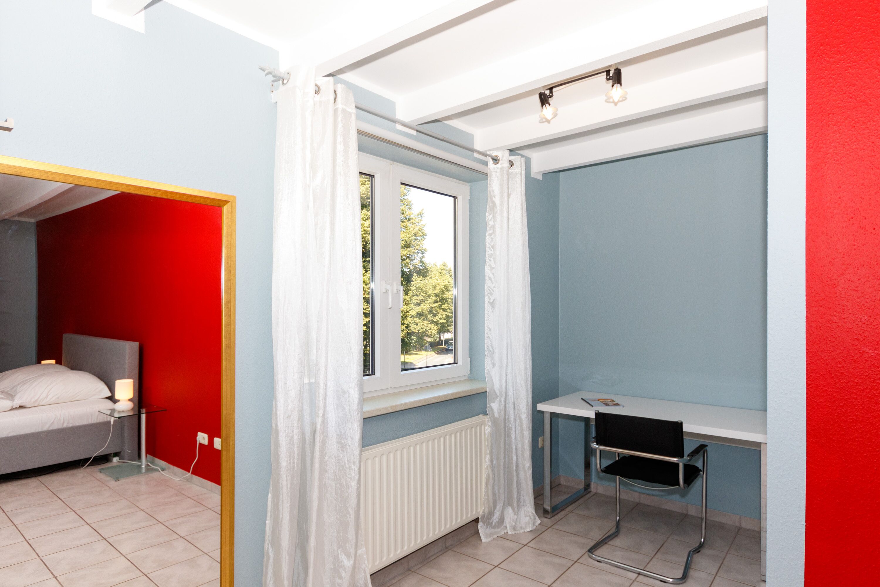 A bedroom with a bed, a desk, and a window with curtains.