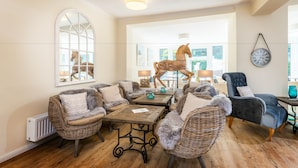A spacious living room with wicker furniture, a horse sculpture, and a clock on the wall.