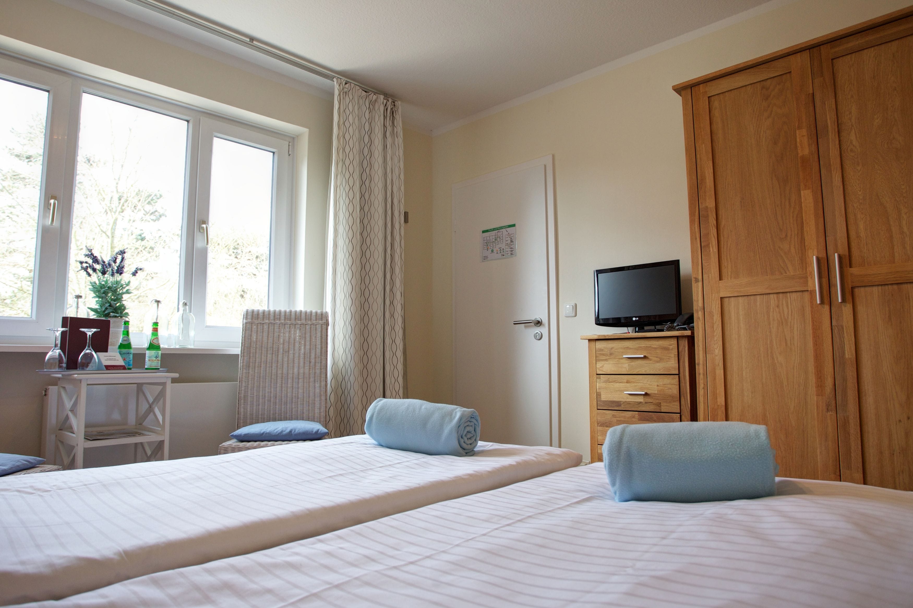 Ein Hotelzimmer mit zwei Betten, einem Fernseher, einem Holzschrank, einem Schreibtisch mit Stuhl und einem Fenster mit Vorhängen.