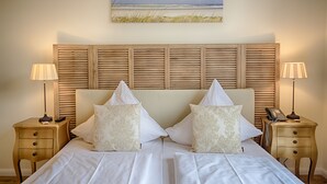 A double bed with a wooden headboard, two bedside tables with lamps, and a painting of a beach scene above the bed.