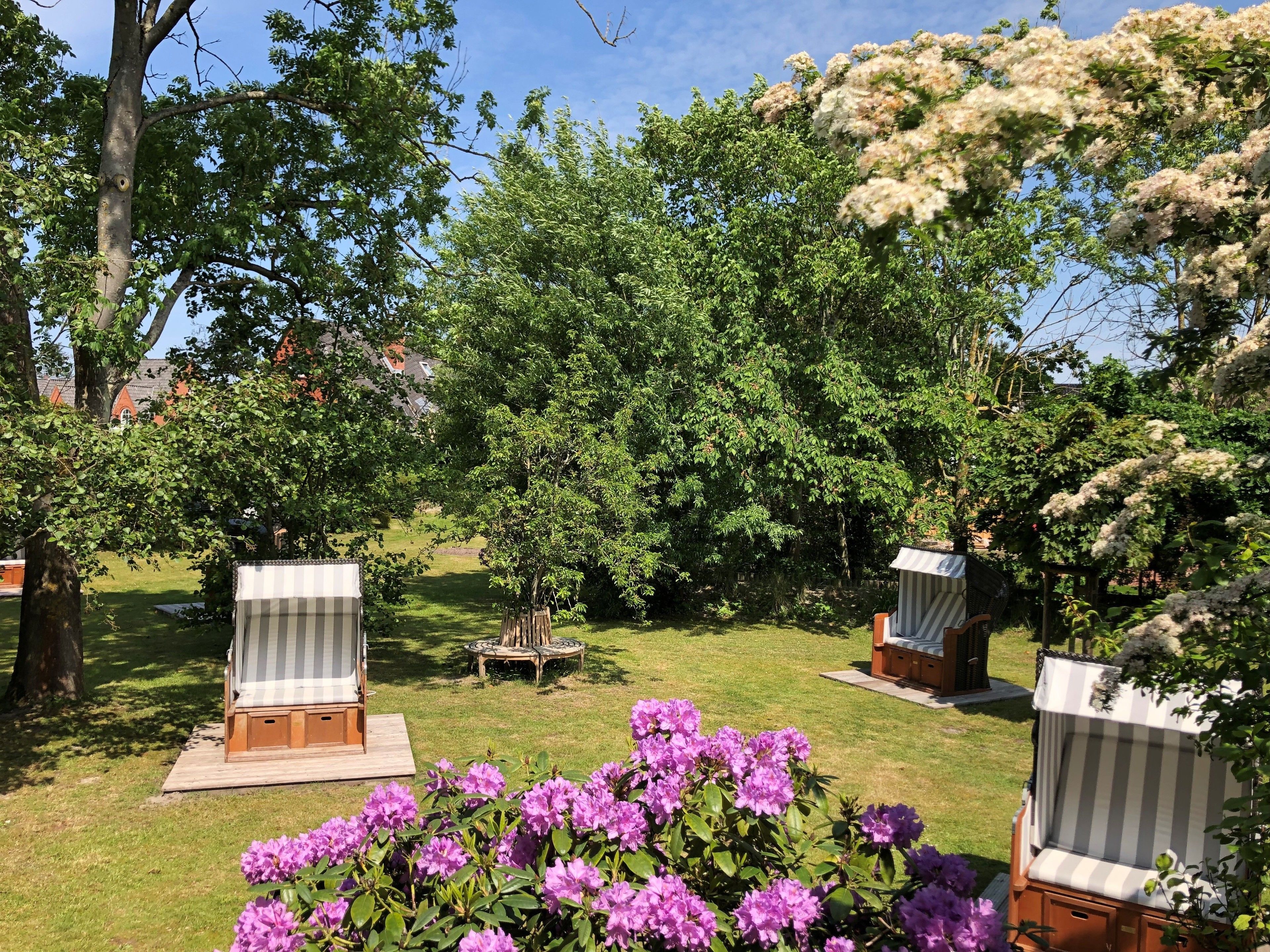 A garden with two striped lounge chairs, a wooden table, and a small wooden structure.