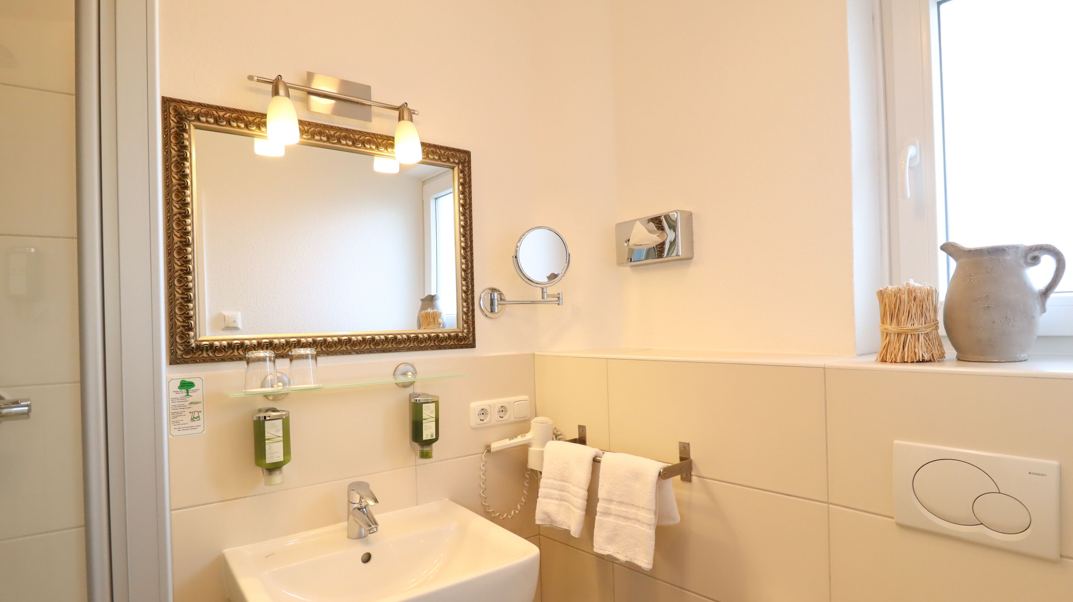 Une salle de bain avec un grand miroir, un lavabo, un porte-serviettes et une fenêtre donnant sur un beau paysage.
