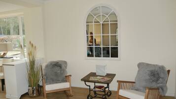 A room with two wooden chairs, a small table with magazines, a window with a view of a statue, and a potted plant.