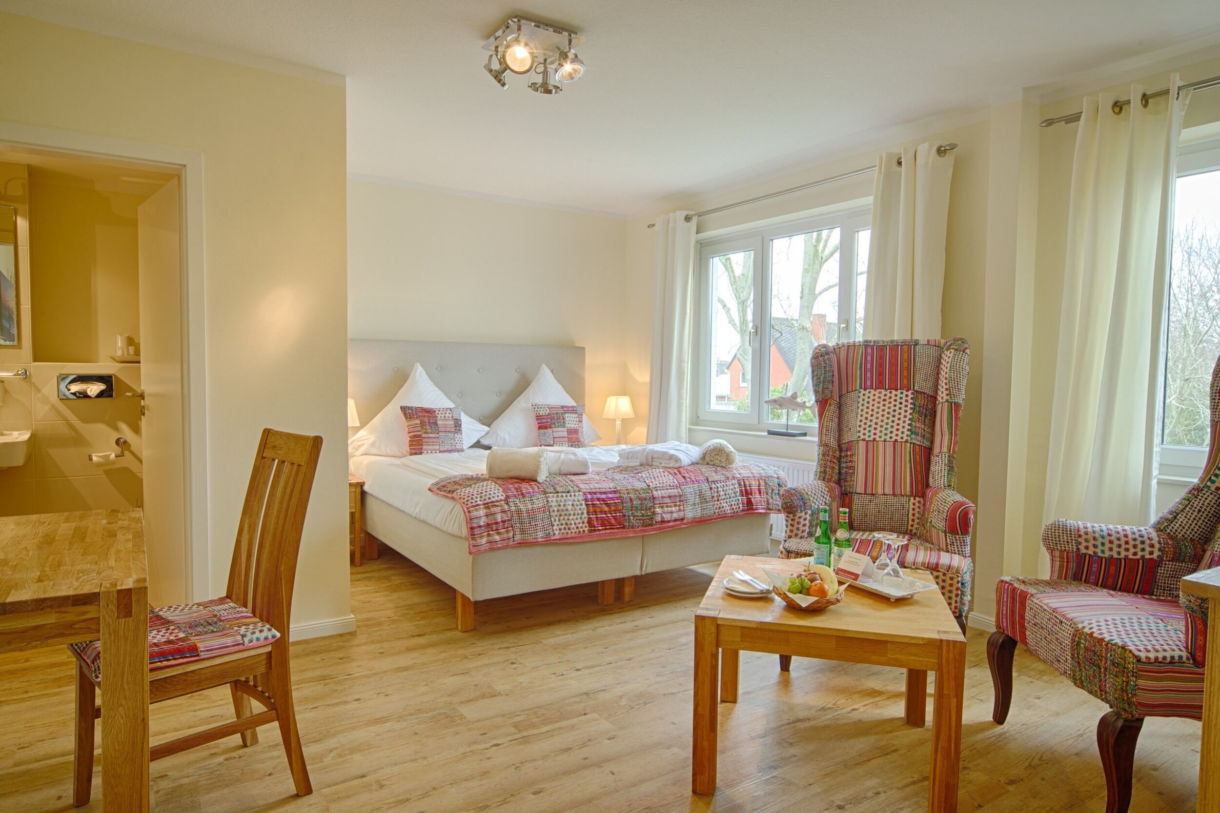 A bedroom with a bed, a wooden chair, a table, and a window with curtains.