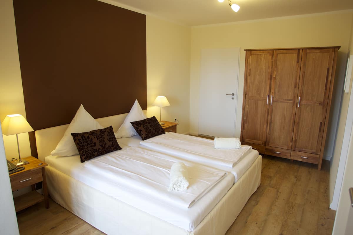 Une chambre d’hôtel avec deux lits, une armoire, un bureau avec une lampe et une table de chevet.