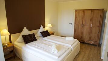 A hotel room with two beds, a wardrobe, a desk with a lamp, and a bedside table.