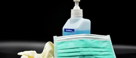 Um frasco de álcool em gel e uma máscara facial sobre uma superfície escura.