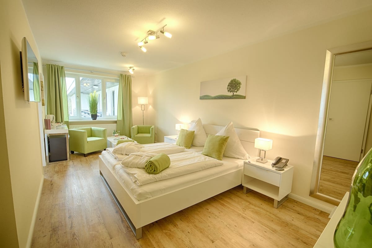 Une chambre d’hôtel avec un grand lit, un bureau, une chaise, une lampe, un miroir et une fenêtre avec des rideaux.