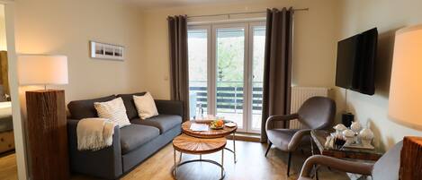 A modern living room with a sofa, two armchairs, a coffee table, and a TV.