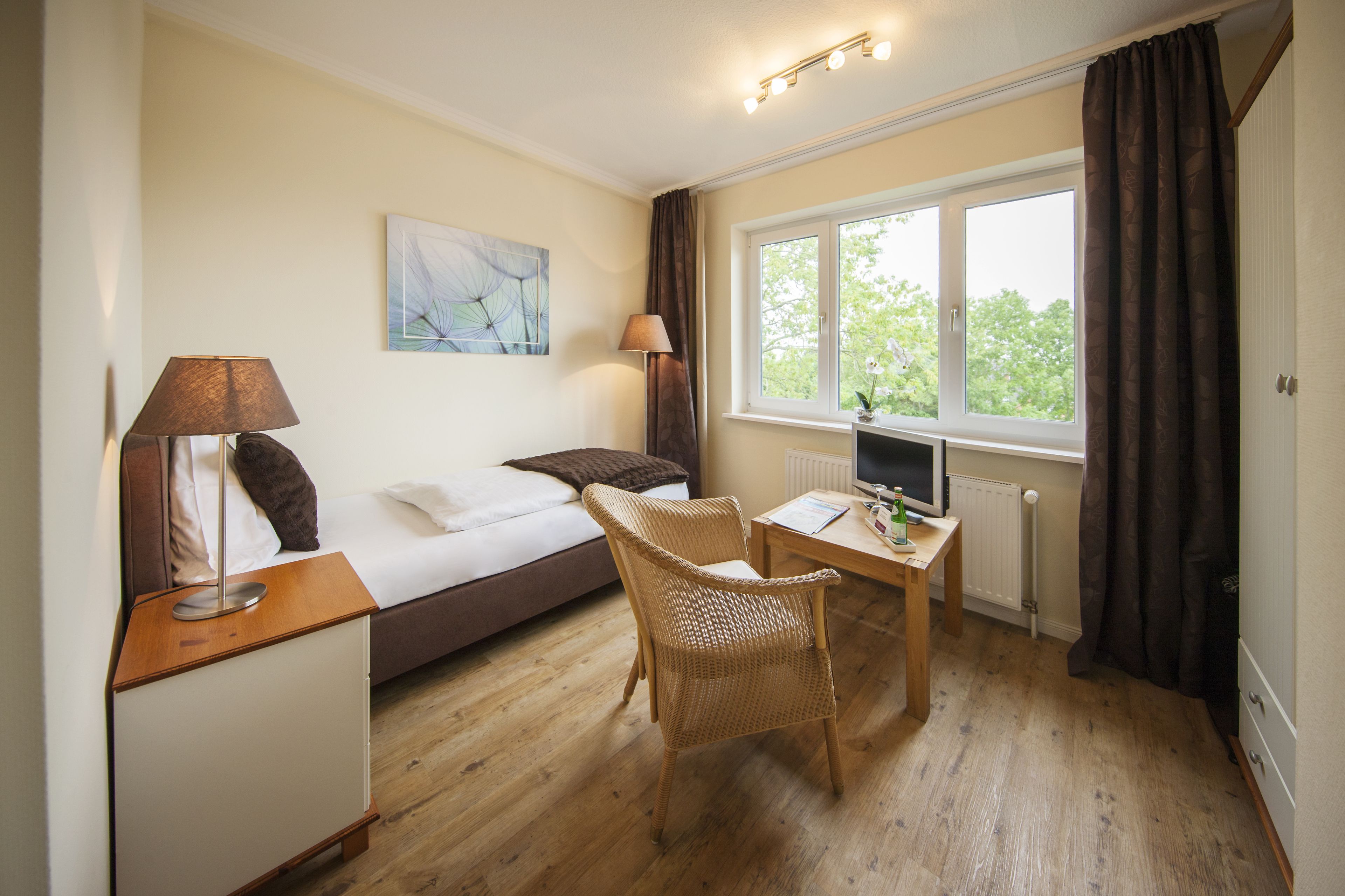 A bedroom with a bed, bedside table, lamp, chair, desk, and window with curtains.