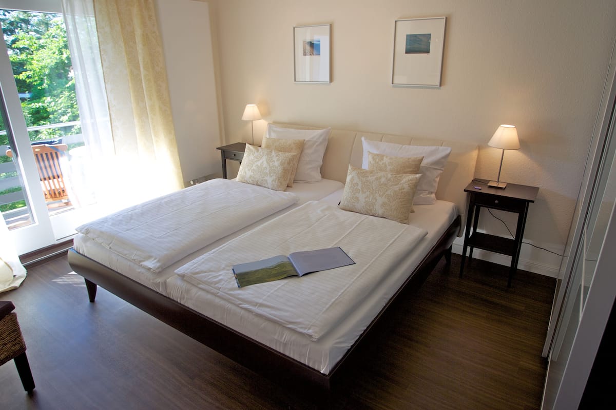 Un lit double avec du linge de lit blanc, deux tables de chevet avec des lampes et deux tableaux encadrés au mur.