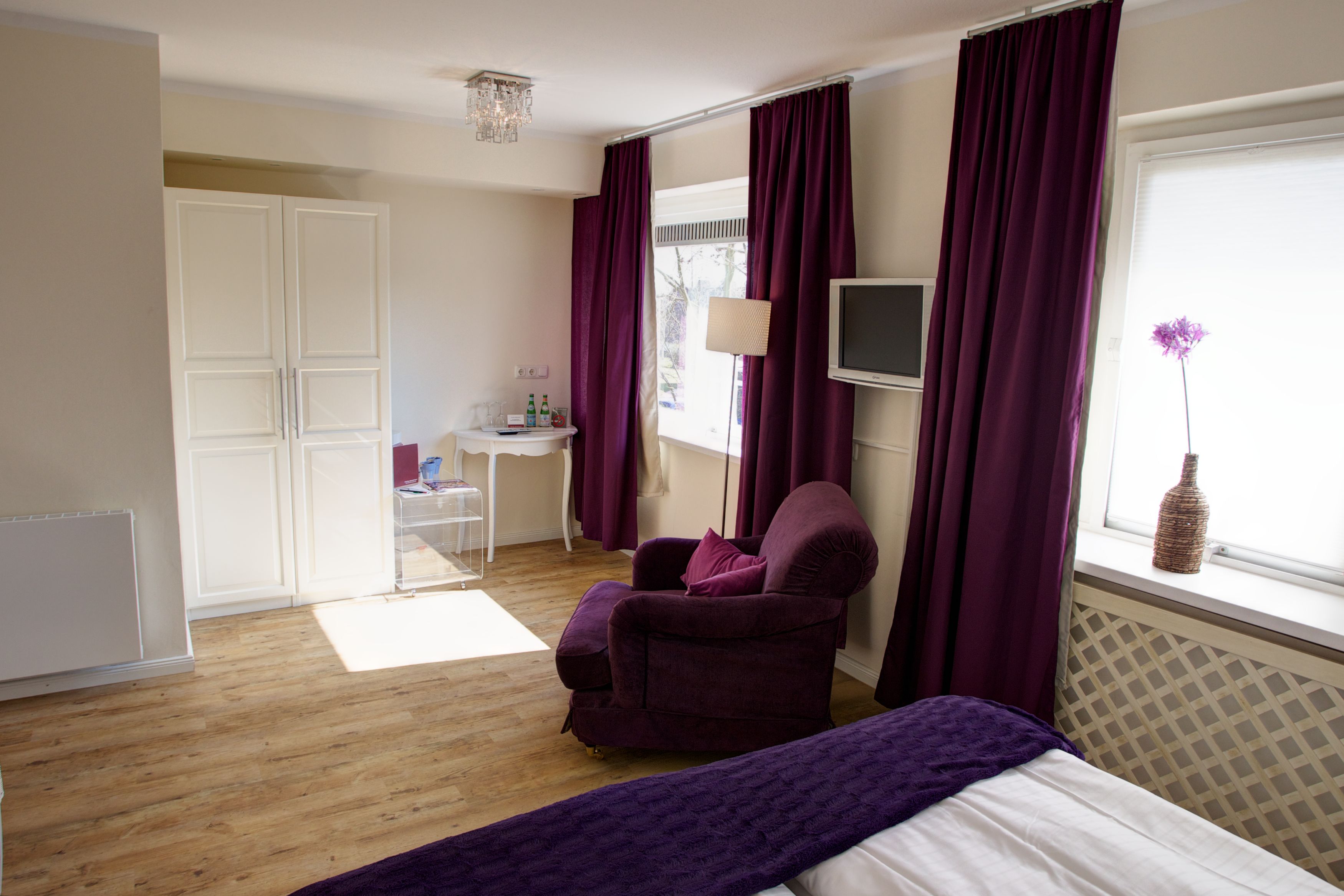 A bedroom with a bed, a chair, a desk, and a window with curtains.
