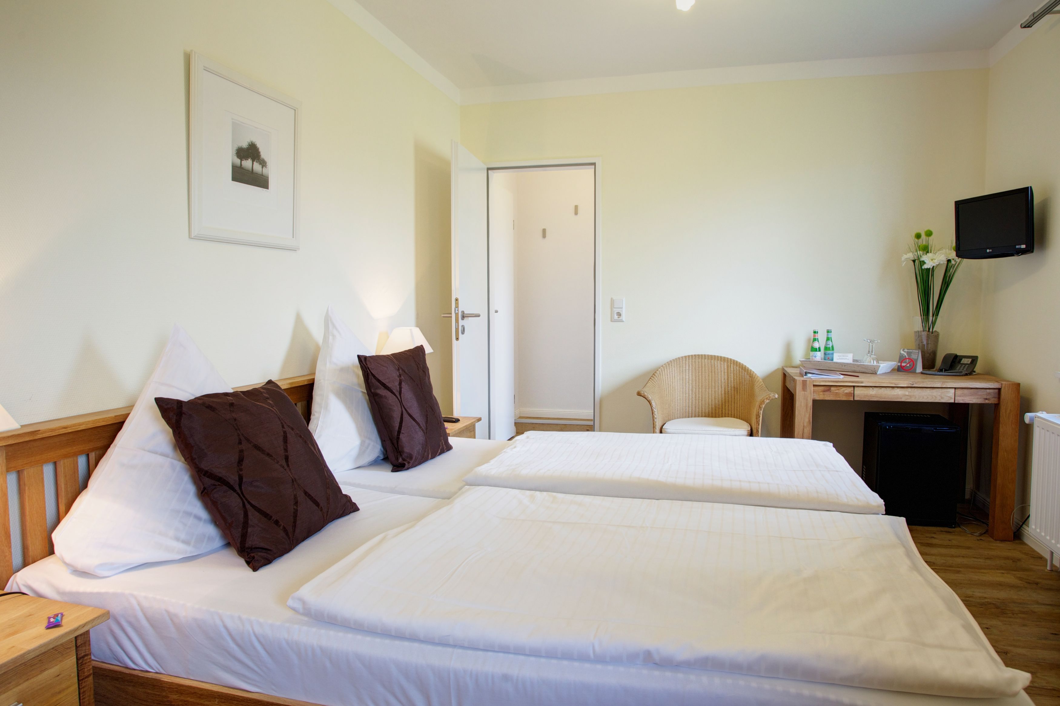 A hotel room with two beds, a desk, a chair, a television, and a door.