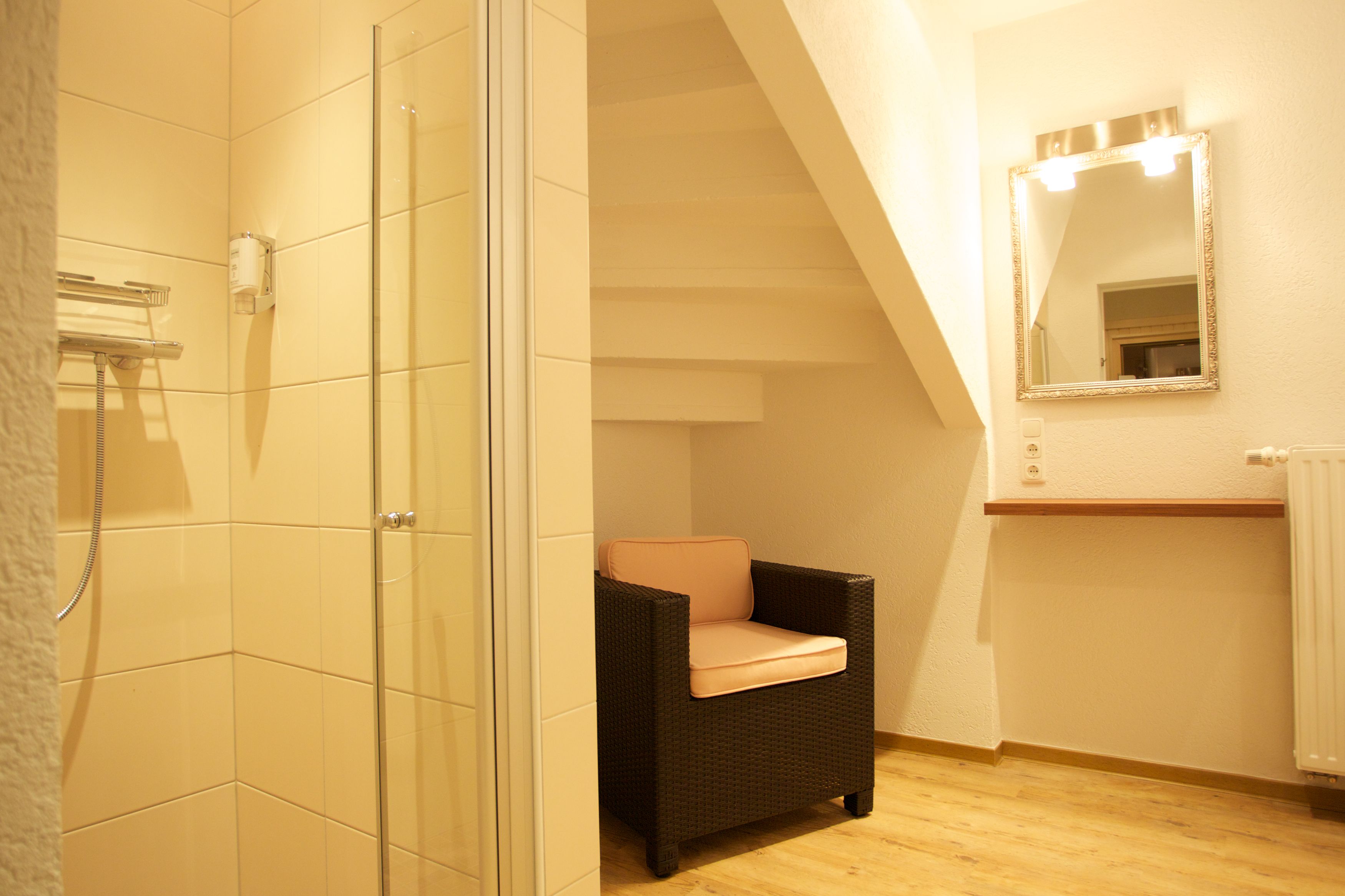 Un baño con cabina de ducha de vidrio, una silla de mimbre, un espejo y un radiador.