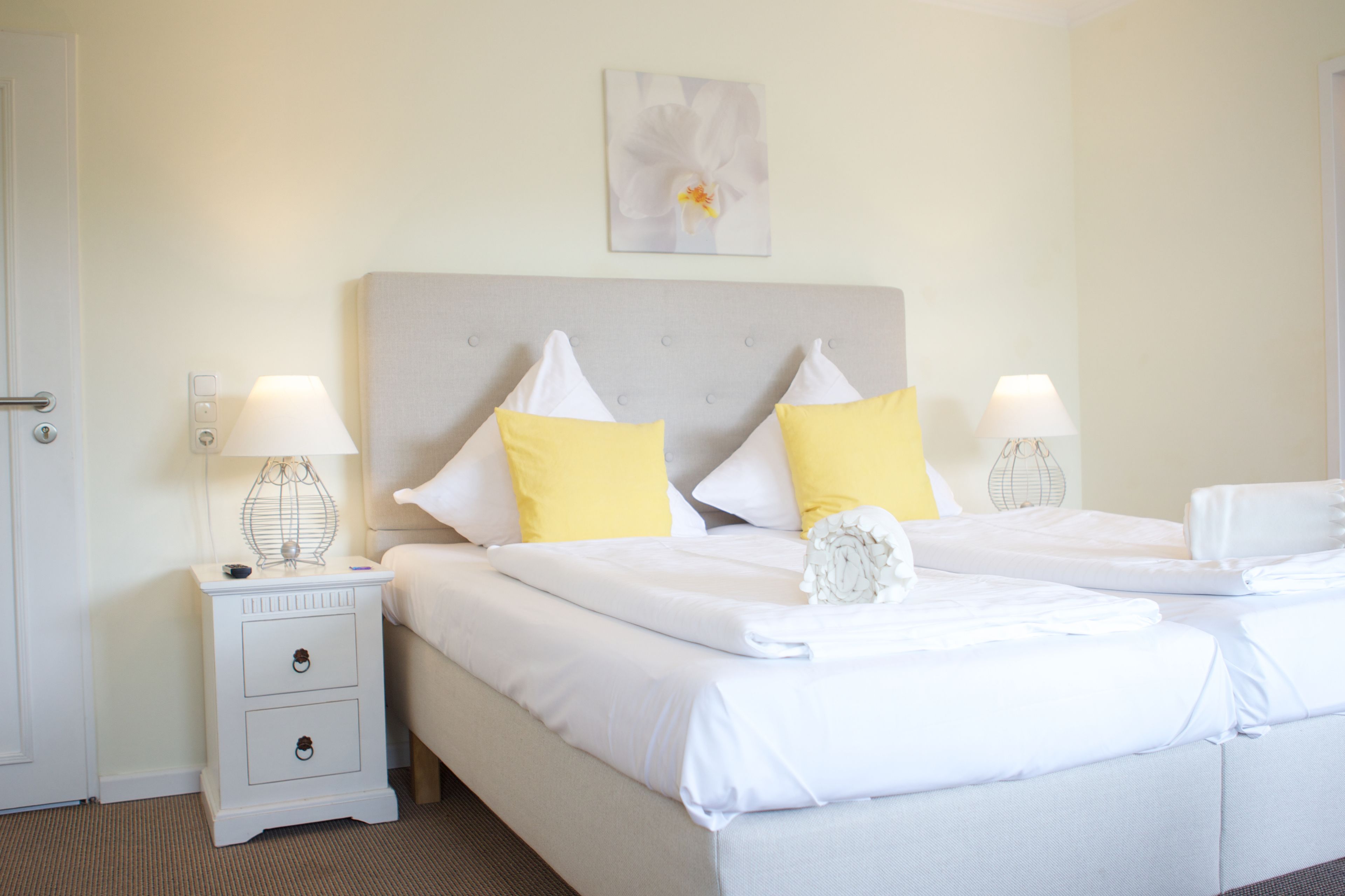 A hotel room with two beds, white bedding, a grey headboard, and a single nightstand with a lamp.