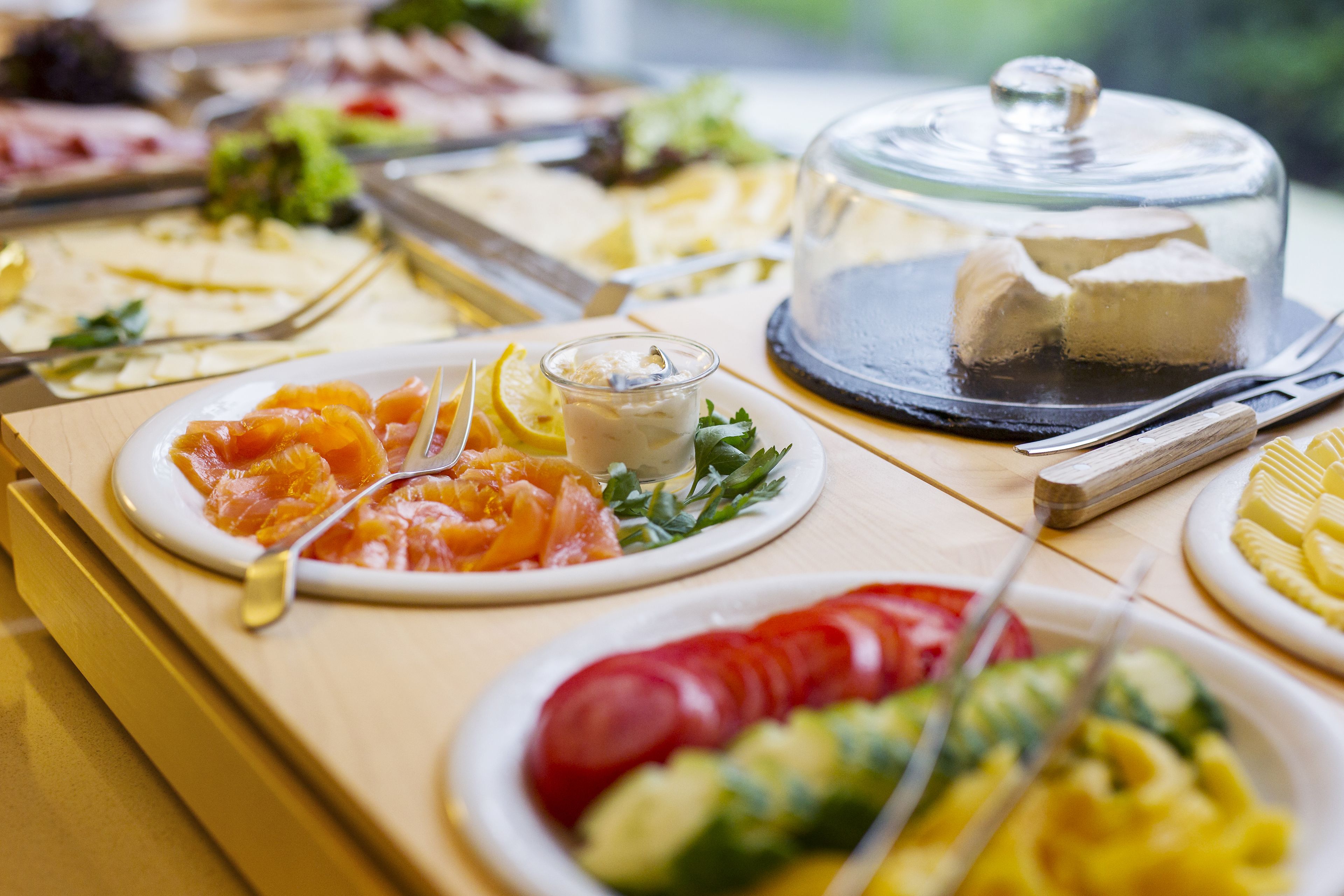 Une table de buffet proposant divers plats, notamment du saumon fumé, un verre de vin blanc et un dessert couvert.