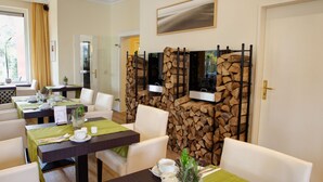A dining area with tables set for two, chairs, a television mounted on a wooden backdrop, and a door leading to another room.