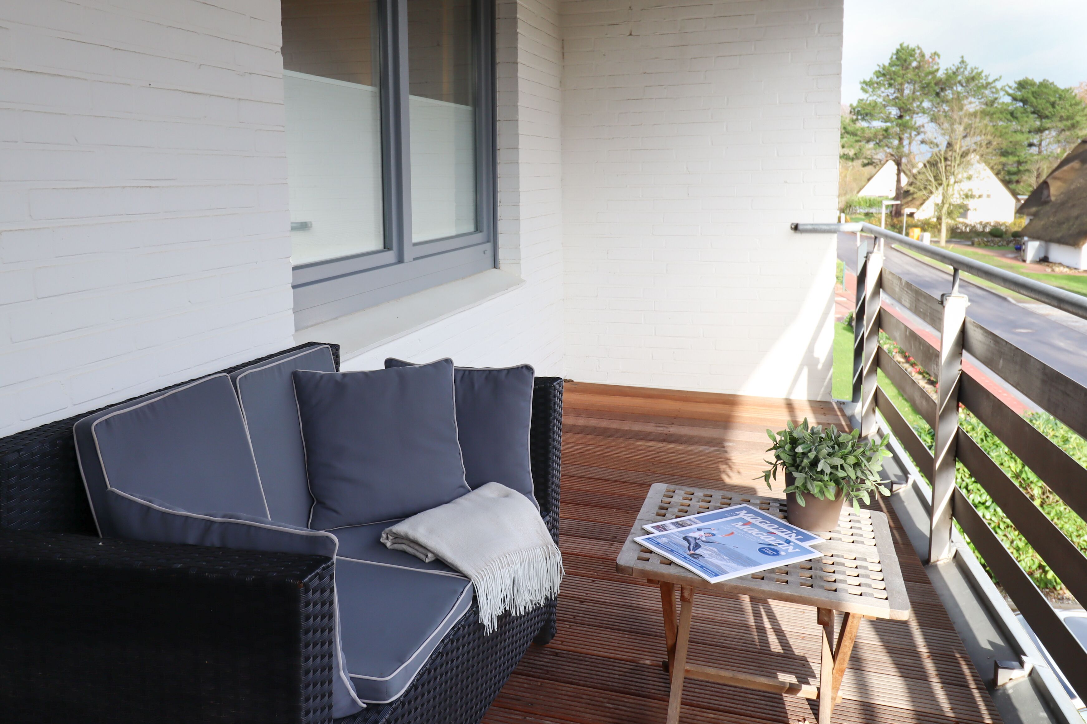 A balcony with a black wicker sofa, a small table with a plant, and a magazine.