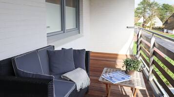 A balcony with a black wicker sofa, a small table with a plant, and a magazine.