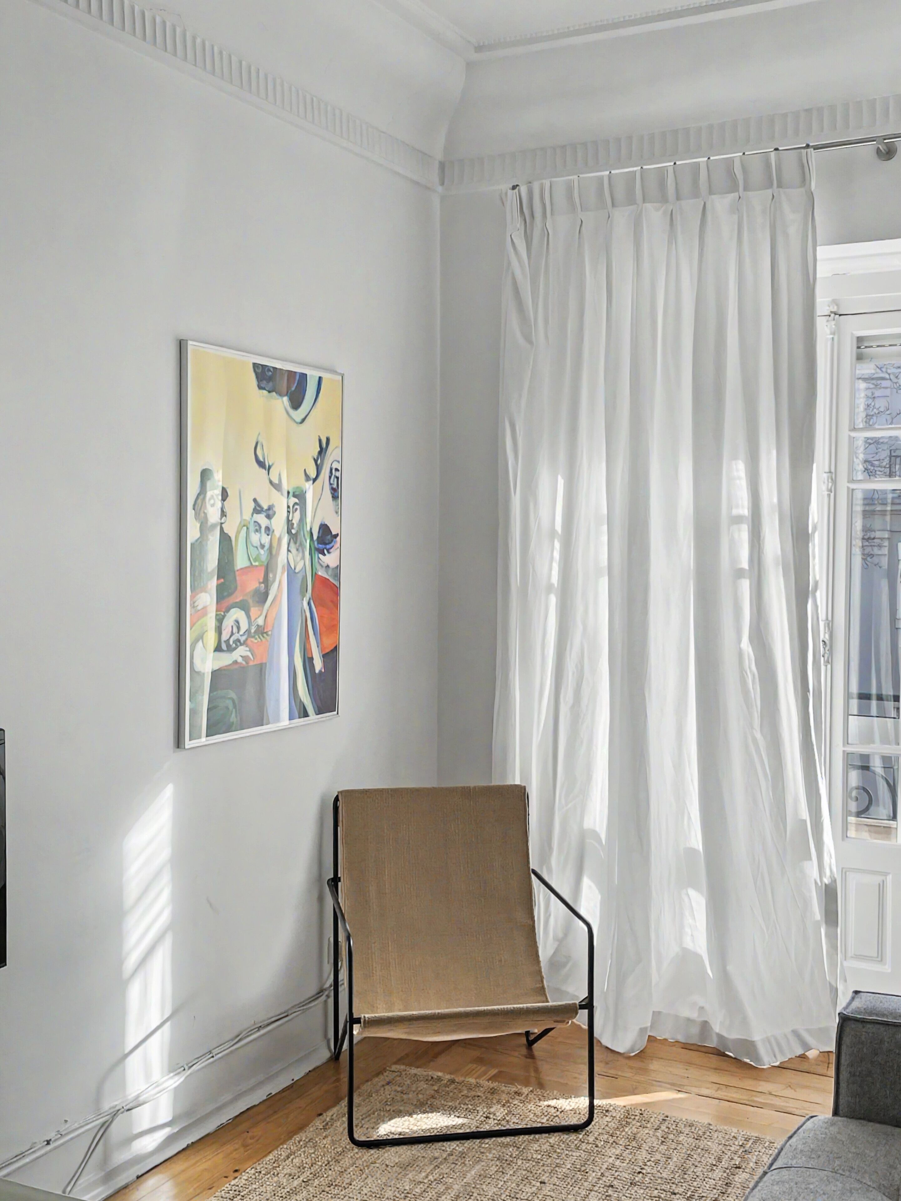 Una habitación con una sola silla, un cuadro en la pared y una ventana con cortinas blancas.