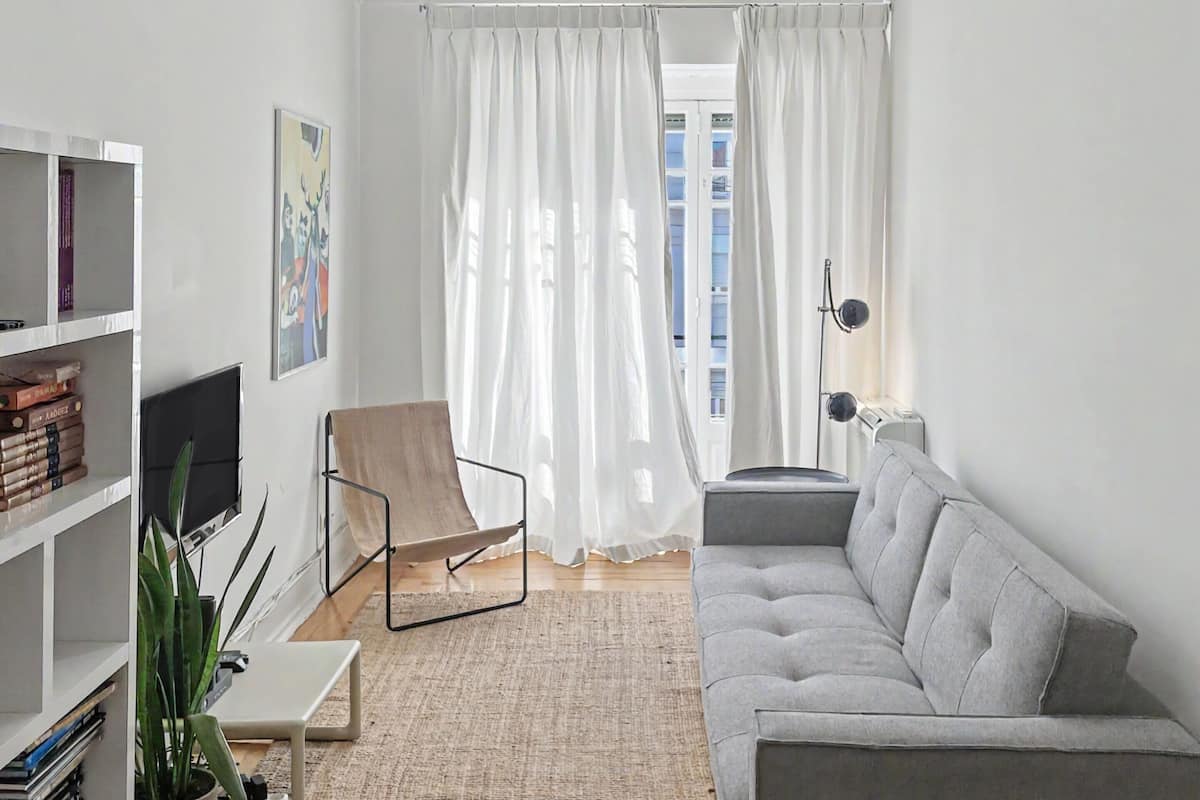 Una sala moderna con un sofá, un sillón, televisor, estantería y una planta en maceta.
