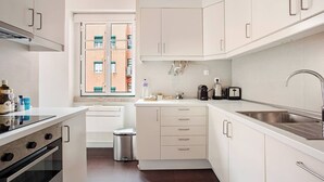 Une cuisine moderne avec des meubles blancs, un évier en acier inoxydable et une fenêtre donnant sur des immeubles.