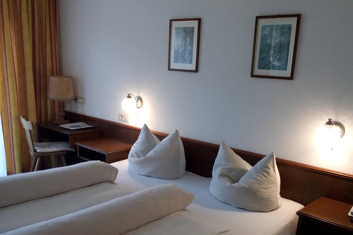 A hotel room with a bed, a desk, and two wall-mounted lamps.