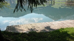 A wooden dock extending into a calm lake with a clear reflection of the sky and surrounding greenery. - Hotel Bernhard am See (Walchsee)