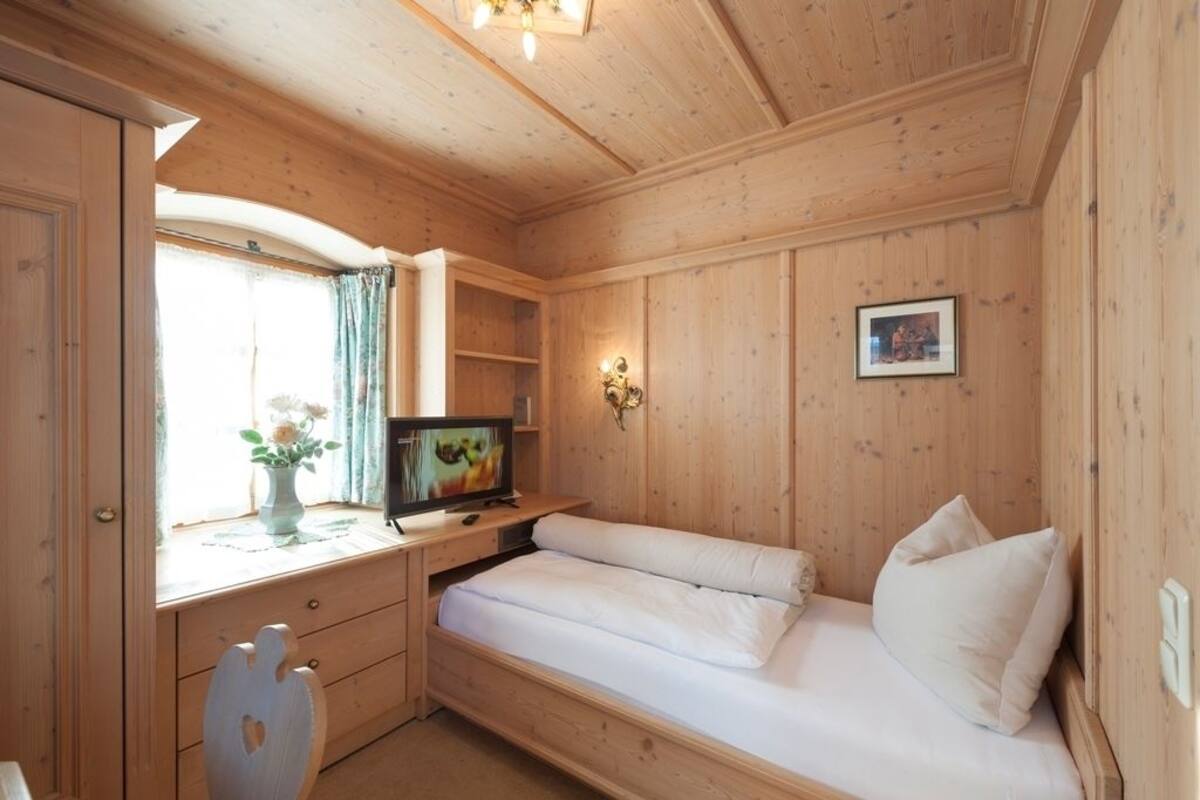 A wooden room with a bed, a desk, and a television.