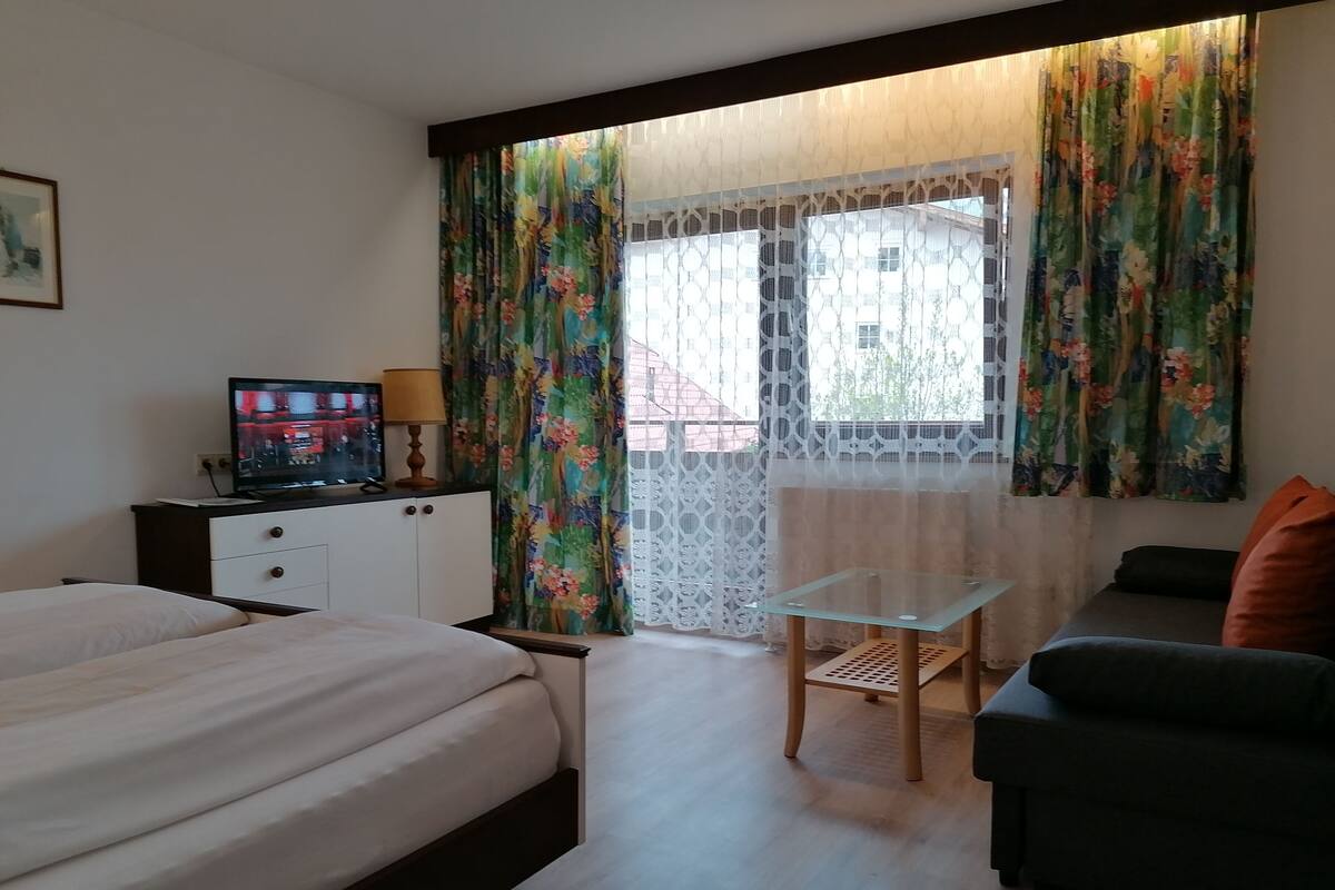 A hotel room with a bed, a desk with a computer, a chair, and a sofa.