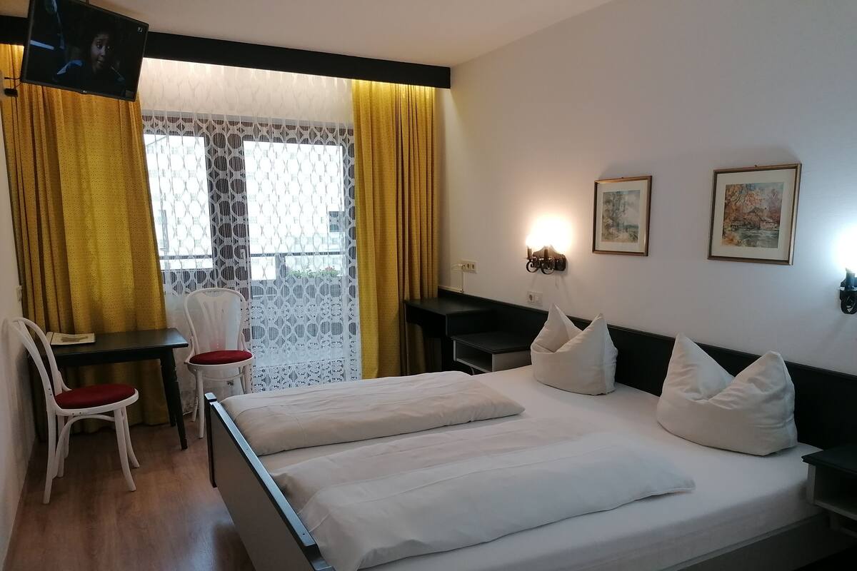 A hotel room with a bed, a desk, a chair, and a TV.