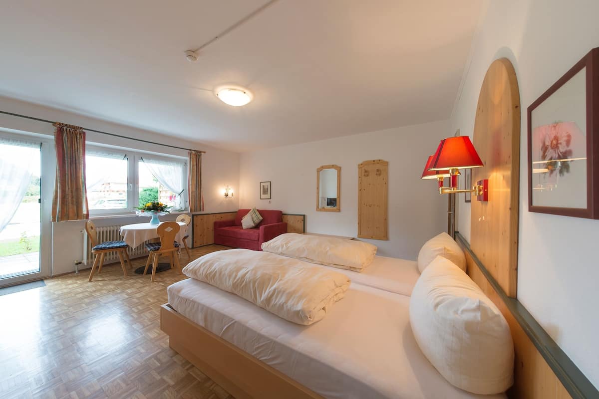Une pièce comprenant un lit, un canapé rouge, une table à manger avec des chaises et une fenêtre avec des rideaux.